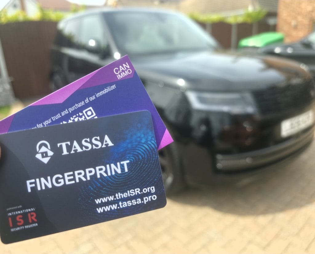 TASSA Fingerprint and CAN IMMO cards held in front of a black Range Rover secured by Elite Car Security